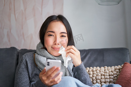 生病的妇女在感冒时通过手机联系她的 GP 的肖像，坐在家里患有流感，使用智能手机