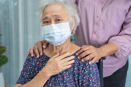 护理人员帮助坐在轮椅上并戴着面罩的亚洲老年或老年老妇人，以保护安全感染 Covid19 Coronavirus。