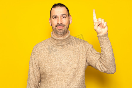 40 多岁有见地、聪明、积极主动的白人男子穿着高领毛衣，举着食指，在黄色背景工作室肖像上提出了一个绝妙的新想法。