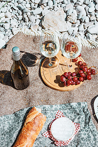 地毯花纹摄影照片_在海岸享受浪漫的乡村野餐，配有两个白酒杯、瓶子、法式面包、卡门培尔奶酪