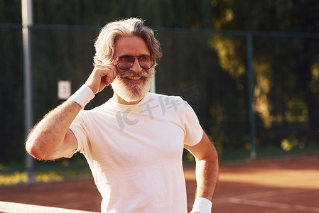 法院灰色服装摄影照片_网球场上戴眼镜、白衬衫和黑色运动短裤的高级时尚男士