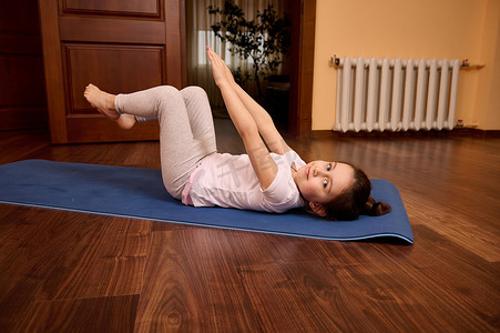 快乐轻松的白人小女孩举起双臂，做腹肌锻炼，伸展身体，躺在健身垫上