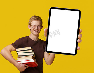 年轻学生手持带有白色空白屏幕的平板电脑，被书籍包围，学习和使用现代技术用于学术目的。