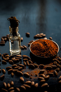 黑色木质表面抗衰老的咖啡面膜，由一些咖啡豆和生有机椰子油组成，装在一个小玻璃瓶中。