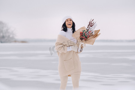 冬花摄影照片_一个穿着米色开衫和冬花的女孩在下雪的季节在大自然中漫步。