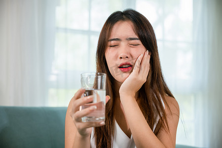 牙齿敏感的亚洲年轻女性拿着一杯冷水