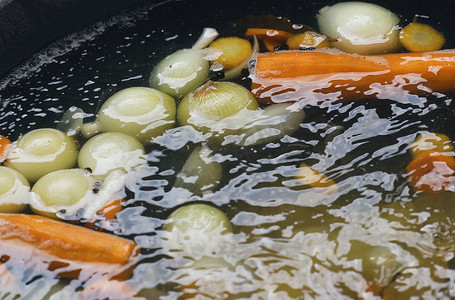 耳朵在锅里煮，洋葱、胡萝卜、香料在水面上可见。