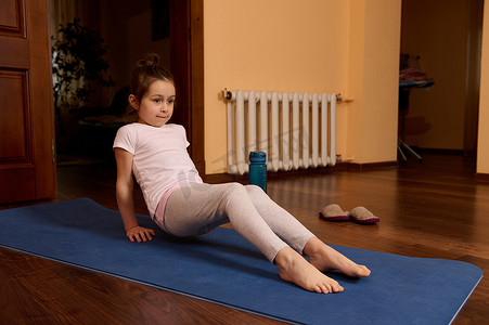 穿着运动服的白种人活跃的运动型小女孩，在室内的健身垫上锻炼。