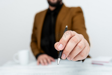 穿着棕色西装的男模特坐在白桌旁，用笔指着重要信息。