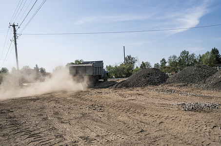 一辆拖车里装着石头的卡车在路上行驶，扬起一片灰尘。