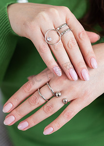 用时髦的浅粉色美甲贴近女性手，佩戴时尚的戒指首饰。