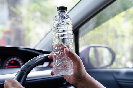 亚洲女司机在车里拿着冷水喝，很危险，有发生事故的风险。