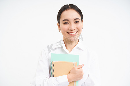 成功的亚洲年轻女性，带笔记本的老师，看起来自信而微笑，白色工作室背景