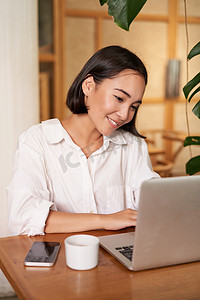 微笑的女经理、自由职业者或学生坐在咖啡馆里用笔记本电脑工作，在电脑上打字