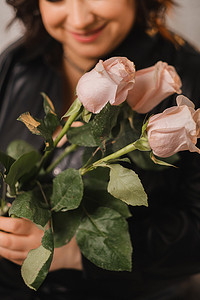 一位穿着黑色皮衣的时尚成年女性站着，室内有一束粉红玫瑰