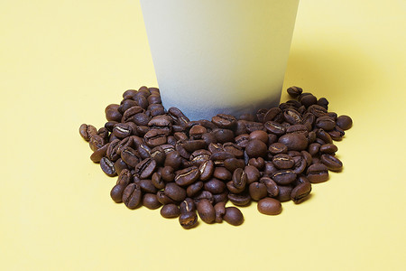 白黄色背景中纸杯旁边的咖啡豆