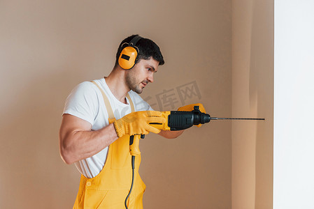 穿着黄色制服的杂工在室内使用锤钻工作。