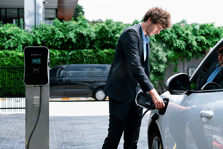 在公共停车场汽车充电站为 EV 汽车充电的进步商人。