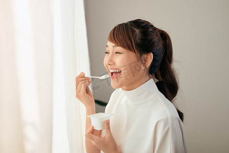窗后吃酸奶的亚洲年轻女性画像