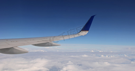 在蓬松多云的天空背景下，从窗户可以看到飞机机翼在云层上方飞行