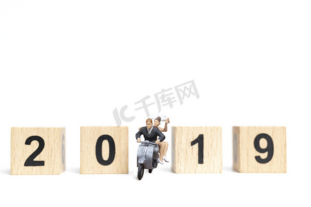 微型人物：2019年，一对夫妇骑着白色背景的摩托车和木块