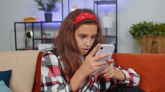 巨大手机摄影照片_家里沙发上的女童使用智能手机打字浏览说哇是的发现了巨大的胜利