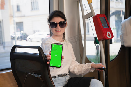 活动绿摄影照片_黑发女人在电车里展示带垂直绿屏的智能手机