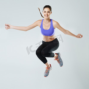 不能碰这个……一个穿着运动服的年轻女子在灰色背景下跳跃的肖像。