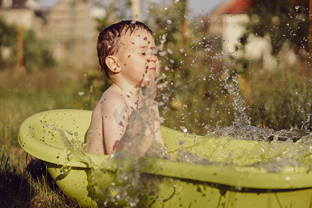 小男孩在洗澡摄影照片_可爱的小男孩在花园里的户外浴缸里洗澡。