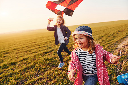 阳光明媚的白天，两个小女孩朋友在田野上玩风筝和玩具车
