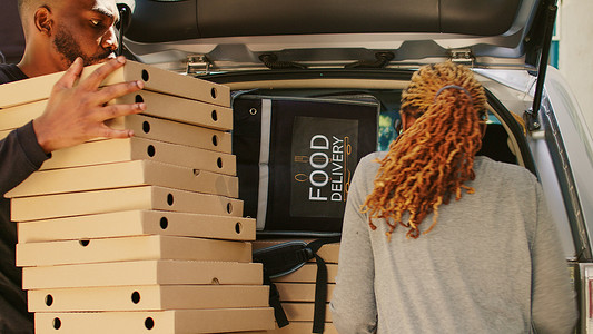 披萨盒摄影照片_非洲裔美国女快递员拿着一大堆披萨盒