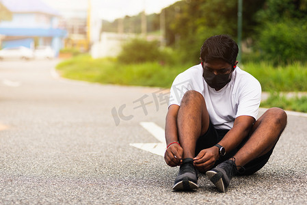 运动赛跑者黑人戴手表坐着他试着系着鞋带跑