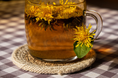 中草药茶摄影照片_桌上玻璃杯中的蒲公英花健康茶。