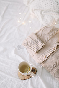 在凌乱的床背景上针织米色毛衣和一杯茶。