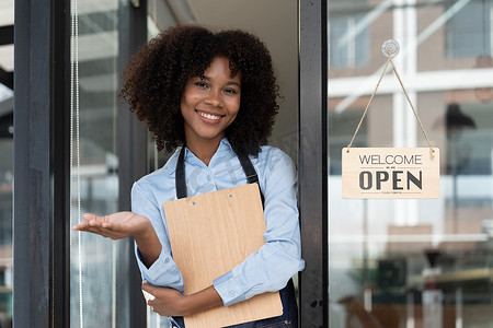 小企业非洲女老板面带微笑，同时转向咖啡馆开业的标志。