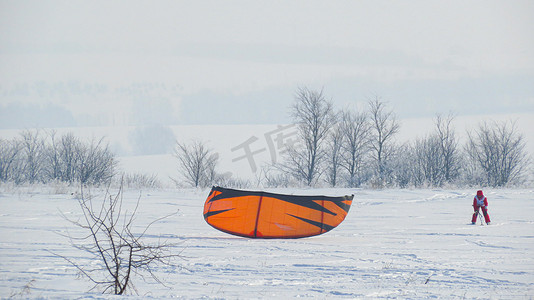 连衣裙子摄影照片_一个穿着红色连身衣、风筝滑雪、冬天在野外跳伞的女孩。