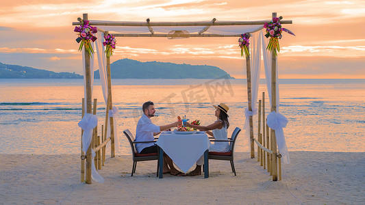 男女喝摄影照片_泰国普吉岛海滩上的浪漫晚餐，一对男女在海滩上共进晚餐