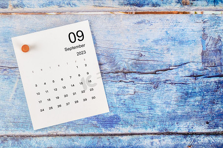 2023 年 9 月的月历和蓝色木质背景上的木制图钉。