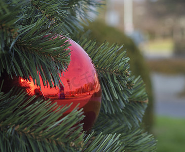 关闭散景去焦城市街道背景上人造圣诞树上的大红色圣诞摆设球装饰