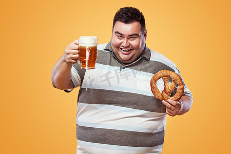 慕尼黑啤酒节上的年轻胖子，喝着啤酒，吃着黄色背景的椒盐卷饼。