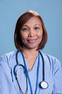 执业摄影照片_在医疗预约期间穿着听诊器和蓝色外套的微笑的执业护士