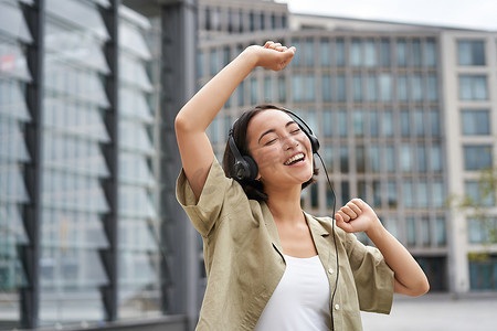 室外音乐摄影照片_女孩戴着耳机在街上跳舞，听音乐，走在城市里感觉很开心