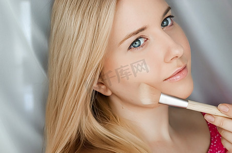 美丽的金发女人用化妆刷在皮肤上涂抹液体化妆粉底