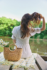 洋湖摄影照片_一位身穿浅色连衣裙的女性背对着镜头坐在湖岸边，拉直她的红发