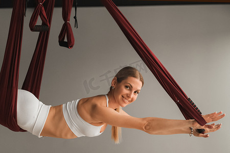 一个穿白色运动服的女孩在健身房的吊床上做瑜伽