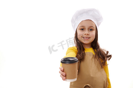 食堂外卖摄影照片_戴着厨师帽和围裙的可爱小女孩，在镜头前拿着一次性纸板杯里的外卖热饮
