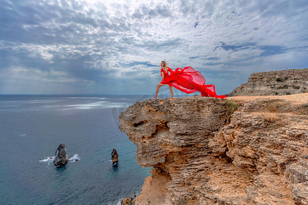 一位身着红色丝绸连衣裙的女子站在海边，背靠群山，她的裙子在微风中摇曳。