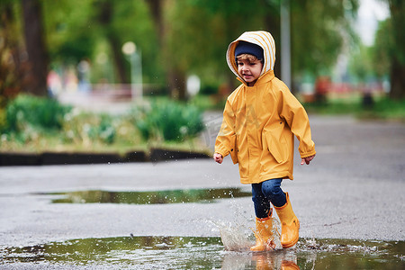 雨后穿着黄色防水斗篷和靴子在户外玩耍的孩子