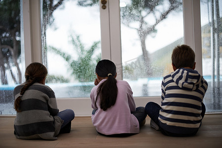 无所事事的雨天...三个孩子在雨天看着窗外的后视照片。