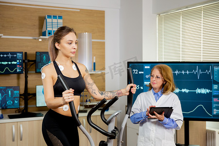 女运动员在踏步机上进行测试，身上有电极，医生跟着她